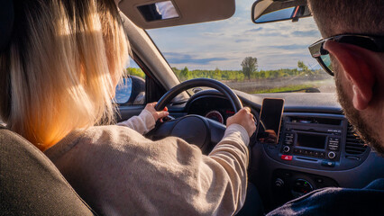 A woman drives a car with an instructor on a sunny summer day. View from the back of the car. A woman learns to drive a car against the backdrop of a beautiful rural landscape.