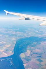 Obraz premium Aerial view from airplane window above green ground. View from the airplane window with beautiful clouds at sunrise