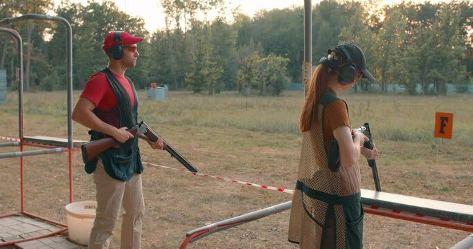 clay shooting enthusiasts having fun outdoors. challenging and thrilling sport. couple wearing cap, protective headphones eyeglasses holding rifles. back rare view. clay pigeon shooting