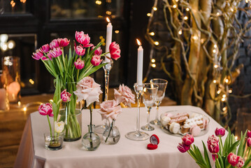 Obraz na płótnie Canvas Table setting in restaurant. Romantic date. Luxury candlelight dinner setup table for couple on Valentine's day. Location decoration tulips flowers, decor candles for surprise marriage proposal.