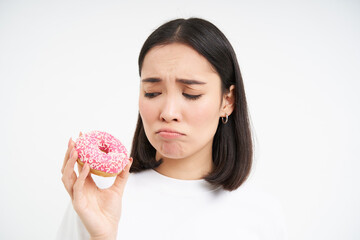 Fototapeta Crying asian woman showing tasty douhnuts and sobbing, being on healthy diet, cant eat junk food, white background obraz