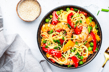 Stir fry noodles with shrimps, paprika, green pea, chives and sesame seeds in bowl. Asian cuisine dish. White kitchen table background, top view