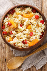 Delicious healthy breakfast millet porridge with dried fruits such as raisins, apricots, cherries close-up in a bowl on the table. Vertical top view from above