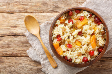 Sweet millet porridge with dried fruits such as raisins, apricots, cherries close-up in a bowl on the table. Horizontal top view from above