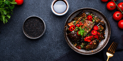Grilled eggplant with red chili peppers, parsley, sesame seed, soy sauce and garlic in asian style, black table background, top view