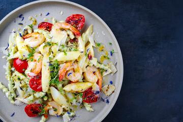 White asparagus glazed with fried king prawns and pistachio pasta served as a top view on a design plate with text space right