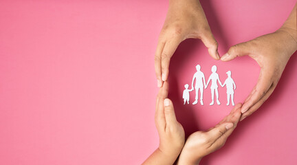 Adult hands make heart symbol around family paper on pink background. health insurance concept,...