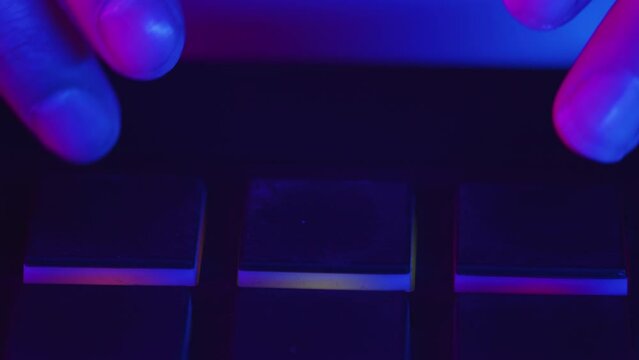 Electronic musician clicks the pads at the controller with both hands making the beat during the studio recording session in a color light close up