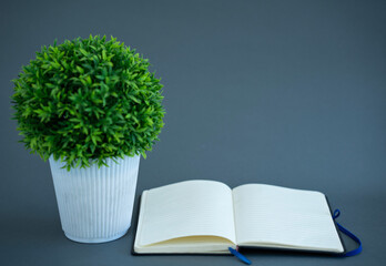 Open blank notebook with artificial green plant, copy space for text