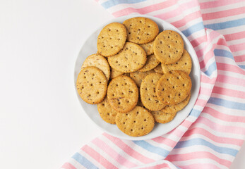 Diet cookies or herbal crackers in white plate and stripped table napkin isolated  top view