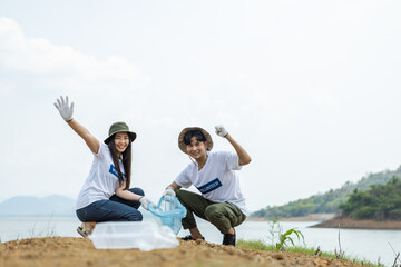 Happy cheerful asian male and female volunteers show hand and collecting garbage, saving world reducing global warming, Volunteers clean plastic bag waste in natural attractions.