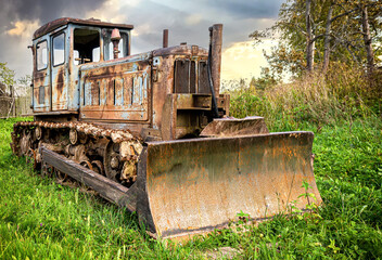 Fototapeta na wymiar Old crawler rusty tractor on the grass at the summer village
