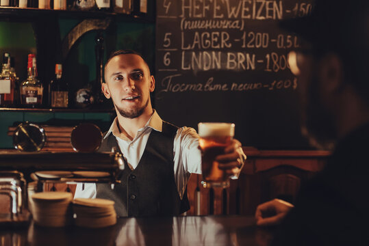 bartender serves a glass of light draft beer to a male guest at bar