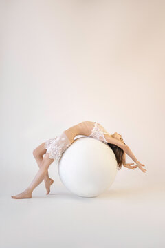 A girl in lace transparent clothes bent over on a large white ball