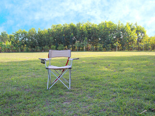 Folding camping chair on the green grass in the park with blue sky background.