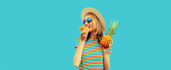 Summer portrait of happy smiling young woman with pineapple and slice of orange, fresh tropical juicy fruits, wearing straw hat, sunglasses on blue background