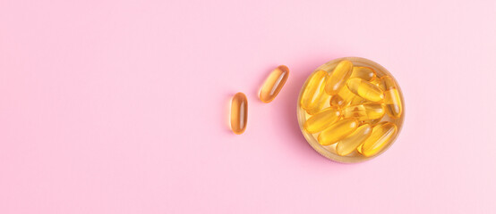 Yellow transparent capsules, fish oil vitamins supplements on pink background. Healthcare, pharmaceutical web banner.  - obrazy, fototapety, plakaty