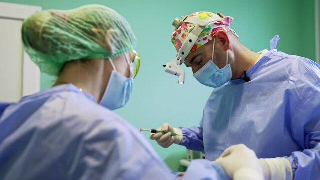 Confident male surgeon takes the electric instrument. Professional plastic surgery specialist performs blepharoplasty.