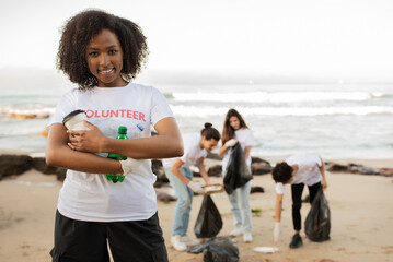 Smiling young african american lady hold bottles and multiracial people volunteers in t-shirts with...