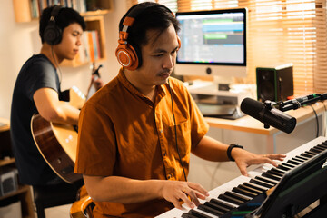 Group of Asian men making music at home studio. He plays guitar and keyboard.