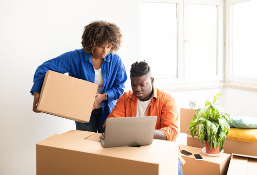 Portrait Of Stressed Black Family Couple Using Laptop While Moving Home