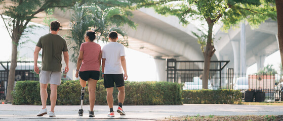 Woman exercising in a park with a friend providing support while using a prosthetic leg. People jogging side by side outside in a park. Female walking and exercise works out outside.