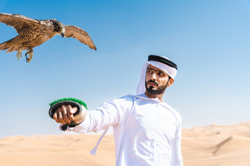 Middle-eastern emirati man wearing arab kandura holding falcon in the desert