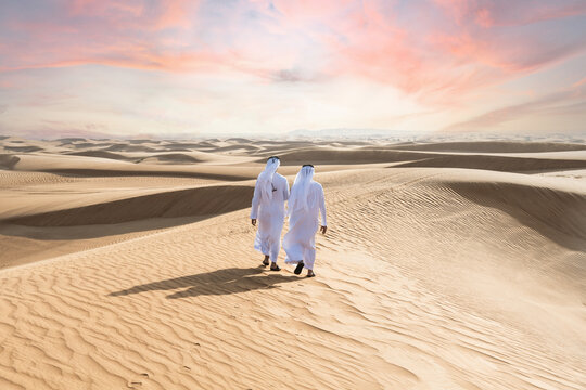 Two middle-eastern emirati men wearing arab kandura bonding in the desert