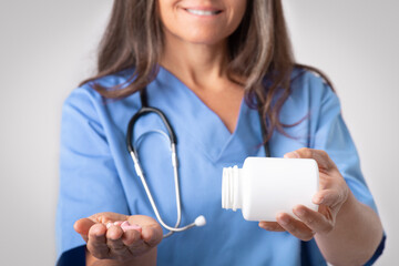 Therapist recommendation. Senior woman doctor in uniform pouring out pills from jar on hand,...