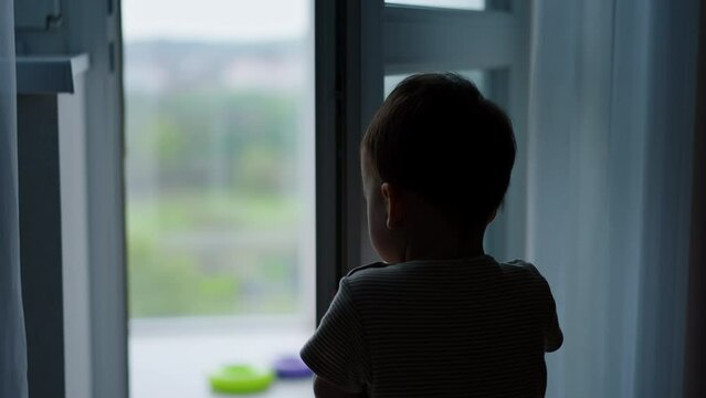 Agile little toddler opens the door. Kid walks to a balcony where his toys are.