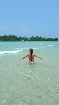 Young happy woman having fun in the sea on a beautiful tropical island during a vacation in slow motion.