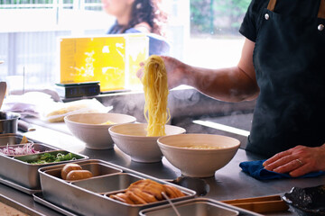 Bowls of ramen on a countertop in a kitchen with steam smoke of boiling noodles, hands put noodles into a bowl with all ingredients to preparing Japanese ramen to serve in a restaurant 