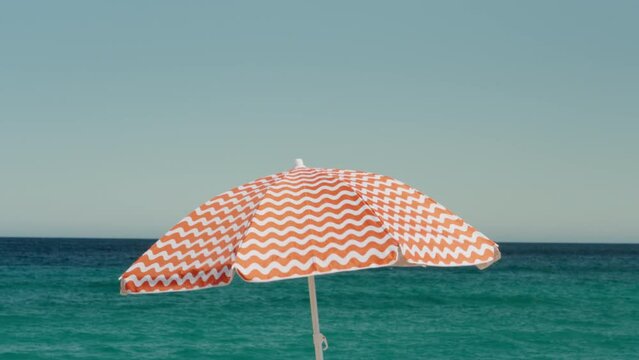Cinematic red and white beach umbrella move in the wind. Summertime vacation concept. Idyllic and simple holiday paradise