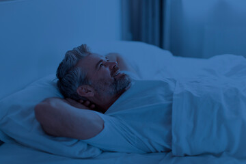 Sleepless middle aged man lying on bed at night