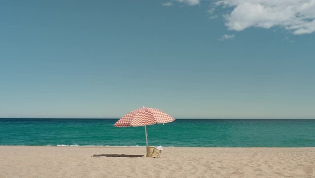 Cinematic minimalistic shot of idyllic paradise empty beach with sun umbrella and woven bag. Peaceful and quiet summer vacation concept. Holiday destination