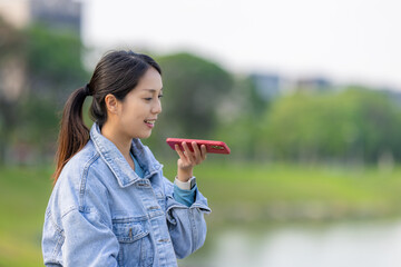 Fototapeta premium Woman send audio message on cellphone at park