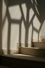 Beautiful spiral staircase made of off white marble and a beautiful artistic diamond shaped shadow on the wall on the side of stairs or in it's background.