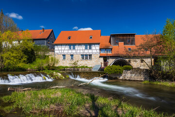 Fototapeta na wymiar Historische Wassermühle in Buchfart am Fluss Ilm in der Nähe von Weimar mit Wasserfall am Wehr
