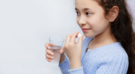 Half-breed child in blue sweater holds a magnesium or calcium tablet in his hand.