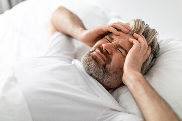 Fototapeta na wymiar Sad middle aged man lying in bed, touching head