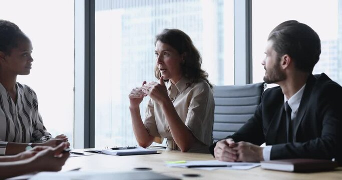 Mature successful businesswoman make speech at group meeting in modern boardroom, give advice to younger workmates, lead formal meeting with partners, discussing new project, reporting result of work