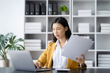 business woman sitting at her desk, reading stats and graphs on paperwork at the office.