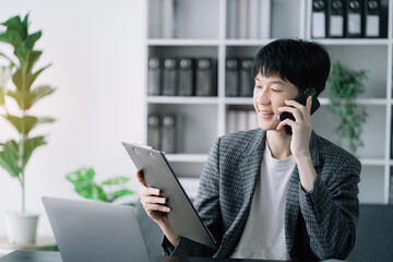 Smiling Asian young freelancer working from home remotely.He is talking on the phone.