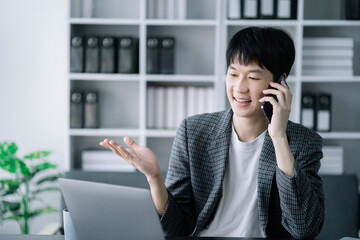 Smiling Asian young freelancer working from home remotely.He is talking on the phone.