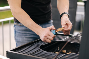 Close-up of human hand hold lighter and lights a fire in BBQ grill on terrace