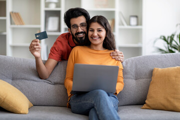 Online Shopping. Happy Indian Spouses Using Laptop And Credit Card At Home