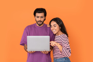 Beautiful young indian couple using laptop on orange, shopping online