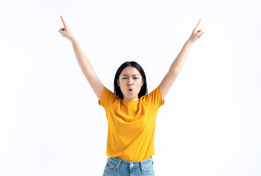 Young excited Asian woman in yellow t-shirt raised her hands up feels a sense of victory, won the lottery, got good news, happy for success standing isolated on white background. Winner gesture