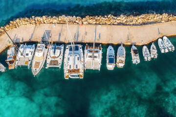 Top view colorful seascape with sailboats and motorboats in sea bay top view. Aerial view of boats and luxury yachts in dock at dawn in summer in Sardinia, Italy. Travel background, clear sea
