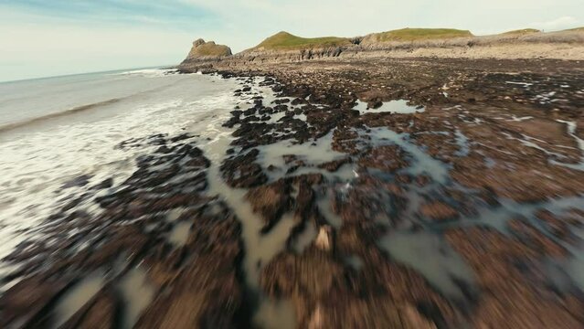 FPV Aerial view of waves crashing onto a rocky coastline at Worm's Head on the Gower peninsula of Wales with a FPV drone